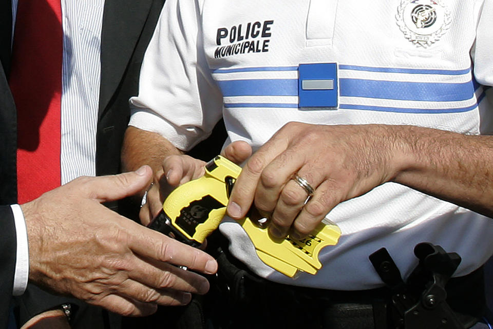 ADDS AN UPDATE FROM THE FRENCH GOVERNMENT - FILE - In this July 10, 2009, file photo, a police officer hands over a Taser to a local politician in Nice, southeastern France. France's government is testing stun guns for wider use after announcing a ban on police chokeholds. The French government later backed away from a complete chokehold ban. (AP Photo/Lionel Cironneau, File)