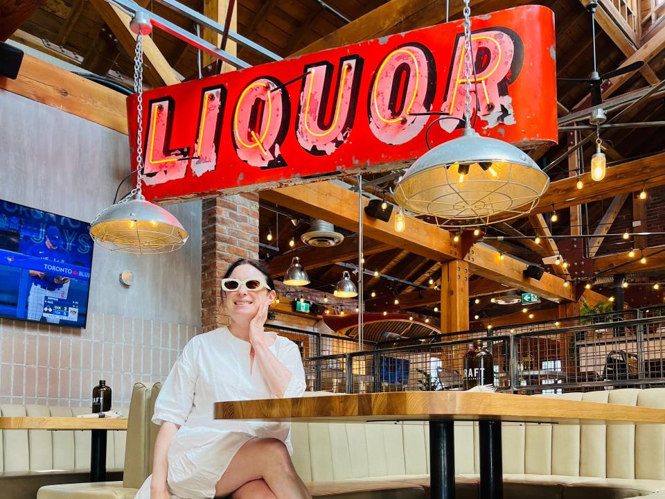 simone posing under a neon sign that reads liquor in a bar in victoria canada