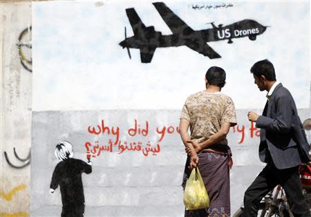 Men look at graffiti showing a U.S. drone on a wall in Sanaa in this November 9, 2013 file photo. REUTERS/Mohamed Al-Sayaghi/Files