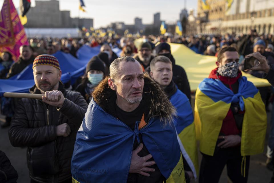 A demonstrator cries listening a national anthem as other rally with Ukrainian national flags in the center of Kharkiv, Ukraine's second-largest city, Saturday, Feb. 5, 2022, just 40 kilometers (25 miles) from some of the tens of thousands of Russian troops massed at the border of Ukraine. After weeks of talks in various diplomatic formats have led to no major concessions by Russia and the U.S., it's unclear how much impact the trips will have. But Ukraine's Foreign Minister Dmytro Kuleba said Friday that "top-level visits seriously reduce challenges in the sphere of security and upset the Kremlin's plans." (AP Photo/Evgeniy Maloletka)