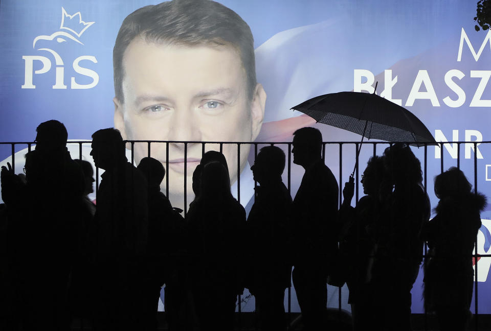 In this photo taken Thursday Sept. 26, 2019 supporters of Poland's ruling right-wing party are standing in line before a candidate's billboard to get to a party convention in Warsaw, Poland, ahead of Sunday parliamentary election in which the Law and Justice party is hoping to win a second term in power. (AP Photo/Czarek Sokolowski)