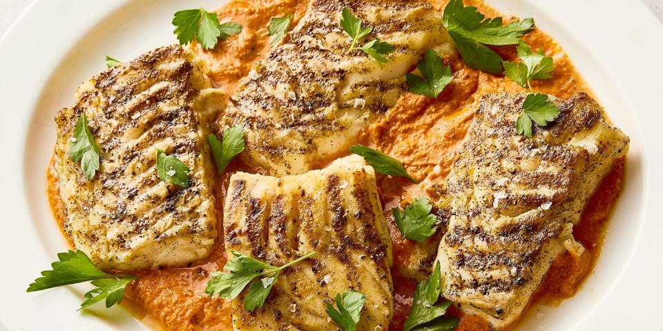 grilled cod on top of a spread of romesco sauce on a white plate topped with herbs