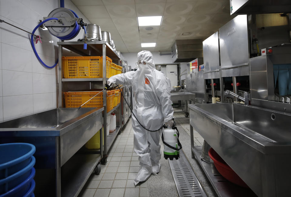 A health official wearing protective gear sprays disinfectant to help reduce the spread the new coronavirus ahead of school reopening in a cafeteria at a high school in Seoul, South Korea, Monday, May 11, 2020. (AP Photo/Lee Jin-man)