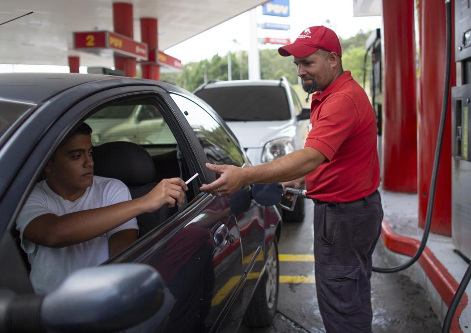 In this Oct. 8, 2019 photo, gas station attendant Leowaldo Sanchez takes a cigarette as payment from a motorist as he fills the tank in San Antonio de los Altos on the outskirts of Caracas, Venezuela. This barter system, while perhaps the envy of cash-strapped drivers outside the country, is just another symptom of bedlam in Venezuela where a full tank these days costs a tiny fraction of a U.S. penny. (AP Photo/Ariana Cubillos)