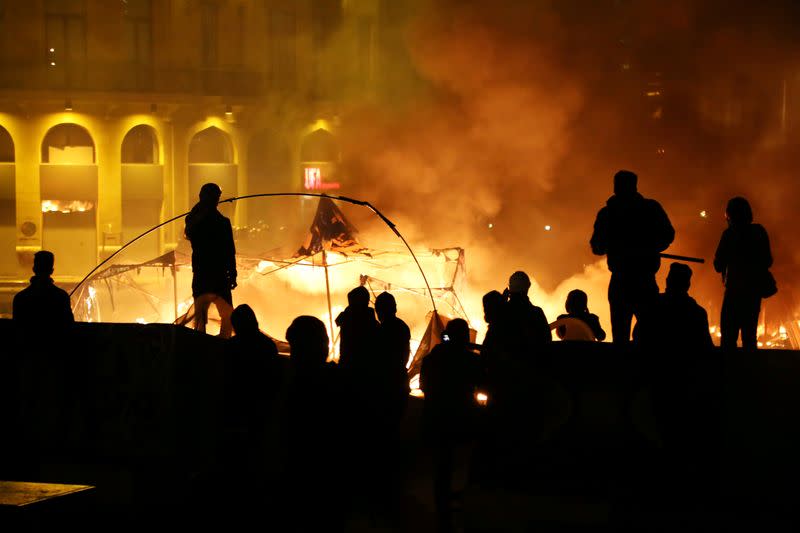 Protesters stand near burning tents during anti government protests in Beirut