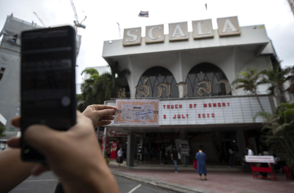 A woman takes a photo of a movie ticket outside the Scala theater Friday, July 3, 2020 in Bangkok, Thailand. The Scala theater has shut its doors after 51 years as a shrine for Thai movie-goers. (AP Photo/Sakchai Lalit)