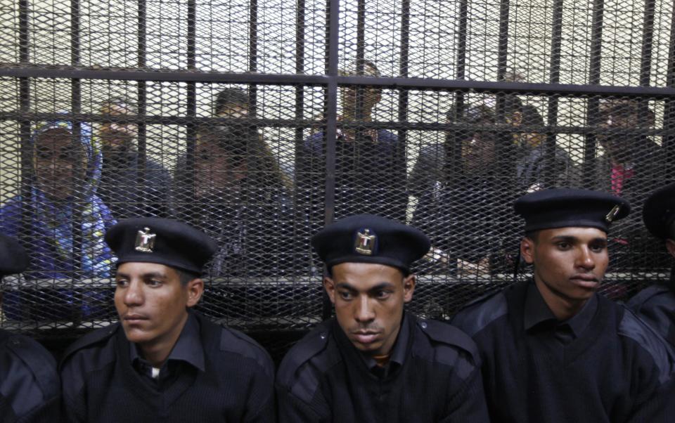 FILE - In this Sunday, Feb. 26, 2012 file photo, Egyptian policemen sit in front of Egyptian employees of several pro-democracy groups charged with using foreign funds to foment unrest during their trial in Cairo, Egypt. Egypt has lifted a travel ban on Wednesday, Feb. 29 for seven Americans charged with fomenting unrest by working for illegally funded pro-democracy groups, signaling an end to the worst crisis in Egypt-U.S. relations in 30 years. (AP Photo/Khalil Hamra, File)