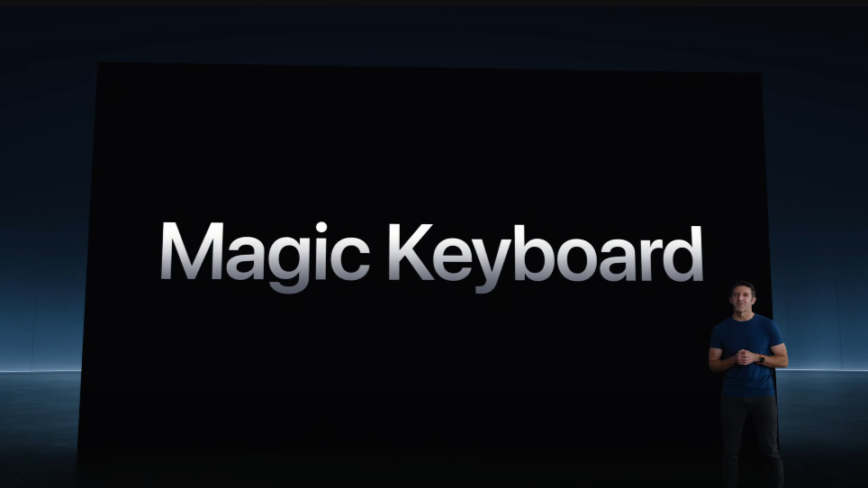  A man standing on a stage with the backdrop announcing the Magic Keyboard in text. 