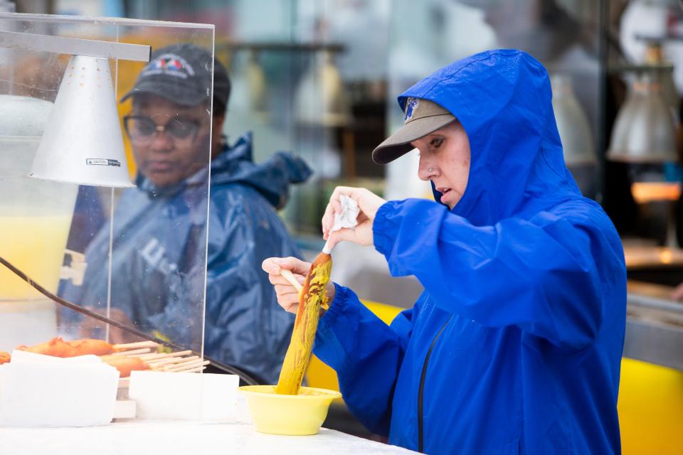 Kelly George lathers a corn dog with mustard while wearing a rain jacket at Pronto Pups at RiverBeat Music Festival on Sunday, May 5, 2024, at Tom Lee Park in Downtown Memphis. The festival began after about a 2-hour weather delay.