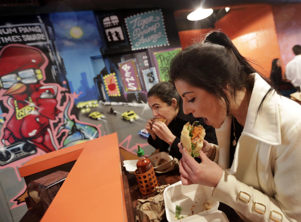 This Dec. 5, 2013 photo shows Krista Agatielli, right, eating at Cambodian sandwich shop Num Pang, near New York's Rockefeller Center. Rockefeller Center is crowded at Christmastime thanks to the famous tree, the skating rink and the show at Radio City Music Hall, but visitors can choose from a variety of places to eat in the area, from ethnic food and street carts to sit-down dining. (AP Photo/Richard Drew)
