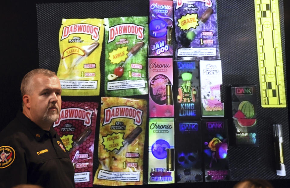 Sgt. Christopher Hannah of the Kenosha County Sheriff's Department stands in front of a display of the colorfully packaged vaping products during a news conference in Kenosha Wednesday, Sept. 11, 2019. (Paul Williams/The Kenosha News via AP)