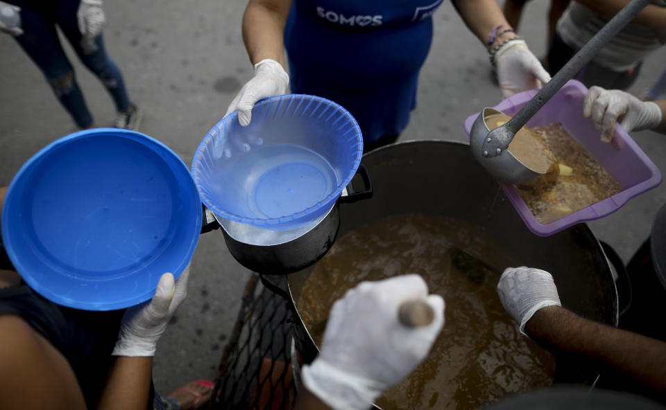 Las personas sostienen recipientes para que sean llenados con guiso de lentejas afuera de un comedor popular en las afueras de Buenos Aires, Argentina, el miércoles 25 de marzo de 2020. (AP Foto / Natacha Pisarenko)