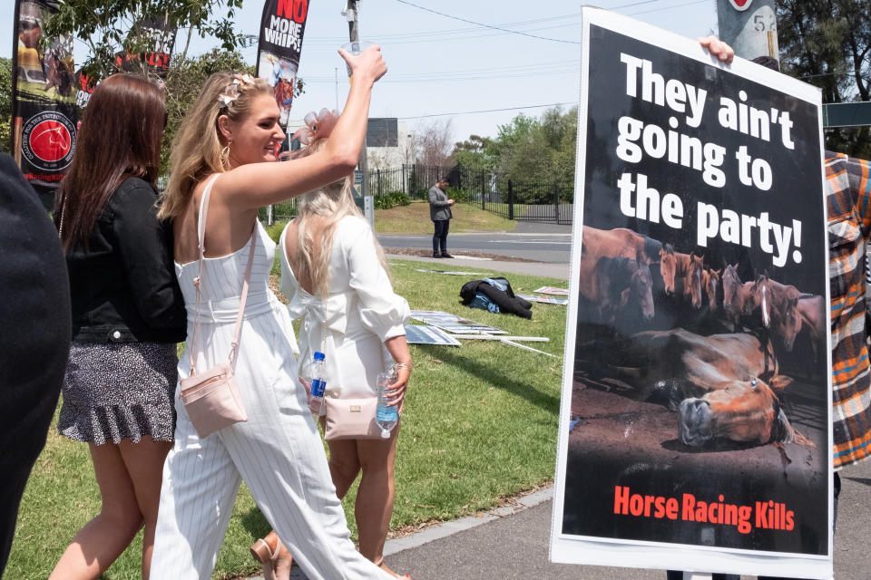 A group of racegoers, pictured here walking past anti-horse racing placards at the Melbourne Cup in 2019.