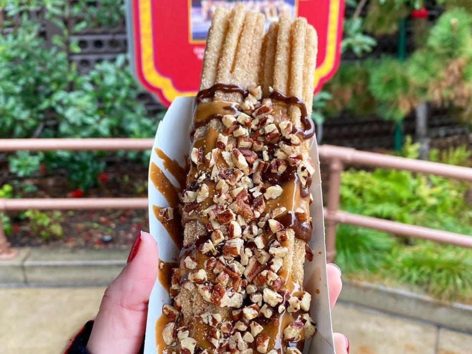 hand holding container of churros covered in chocolate and peanuts