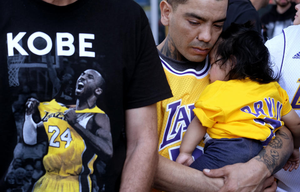 Erik Dominguez holds his 11-month-old daughter Isabella while watching the live stream of a public memorial for Kobe Bryant and his daughter, Gianna, outside the Staples Center in Los Angeles, Monday, Feb. 24, 2020. (AP Photo/Ringo H.W. Chiu)