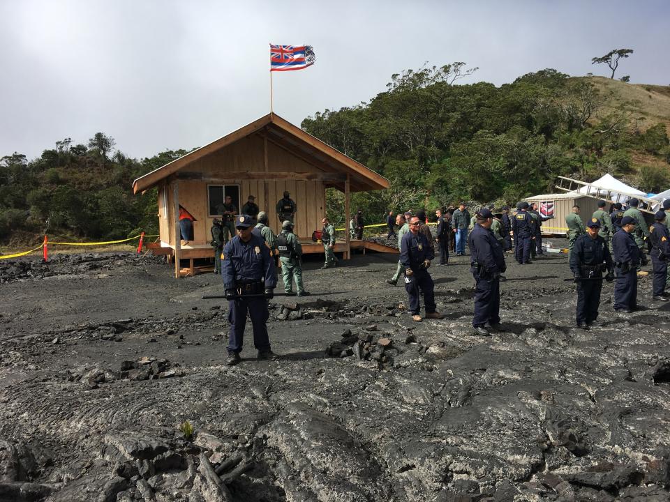 Crews and police gather at a lava field on Hawaii's Mauna Kea on the big island on Friday, Sept. 6, 2019 while a small wooden house is demolished. Opponents of a giant telescope built the unpermitted structure near their protest camp. (Dan Dennison/Department of Land and Natural Resources via AP)