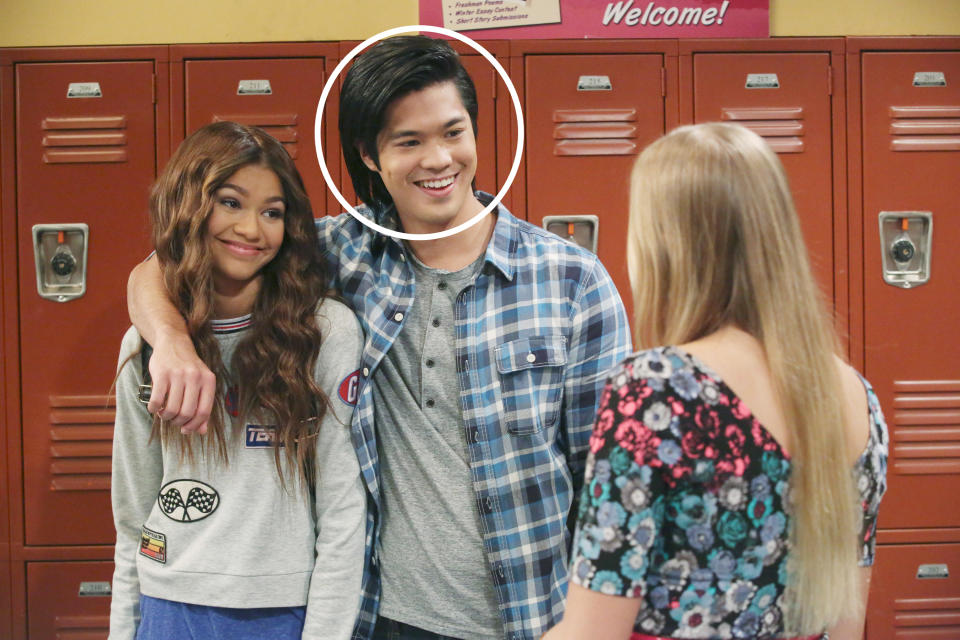 Ross Butler and Zendaya standing by lockers and smiling at a girl with blonde hair