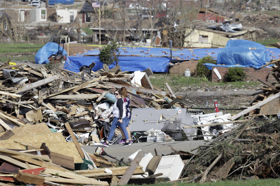 In this March 26, 2020, photo, people walk down a street lined with tornado debris in Gallatin, Tenn. Thousands of people in Middle Tennessee affected by the deadly twisters of March 3 now also have to confront life in the age of coronavirus. (AP Photo/Mark Humphrey)