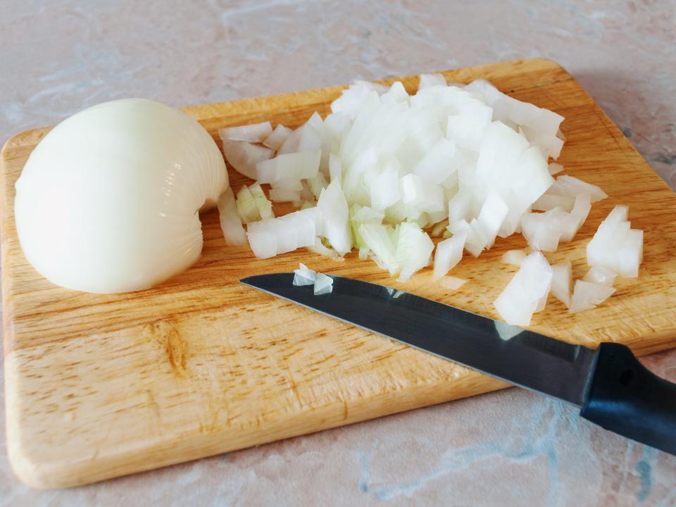 white onion half on cutting board beside chopped onion and knife