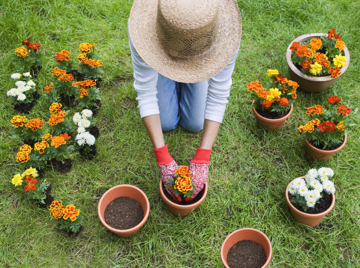 A woman kneeling on the grass with flowerpots around her.