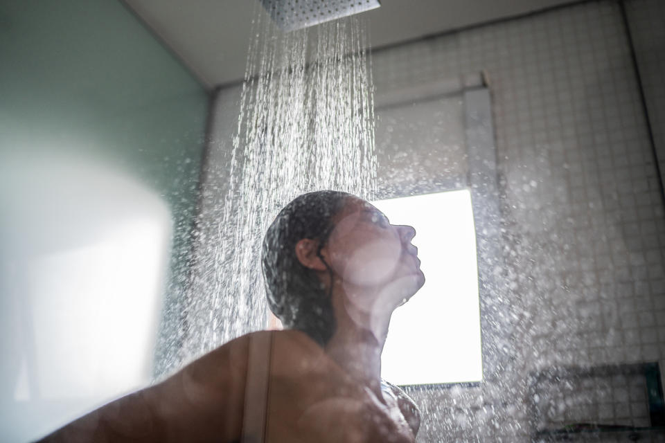 A person enjoying a shower, water streaming down, facing away from the camera