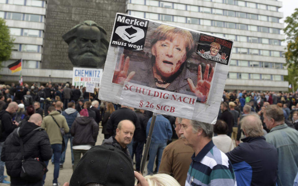 A protestor holds a poster with a photo of Angela Merkel reading 'Merkel must go" and referring she is guilty of incitement in Chemnitz, eastern Germany, Saturday, Sept. 1, 2018, after several nationalist groups called for marches protesting the killing of a German man last week, allegedly by migrants from Syria and Iraq. (AP Photo/Jens Meyer)