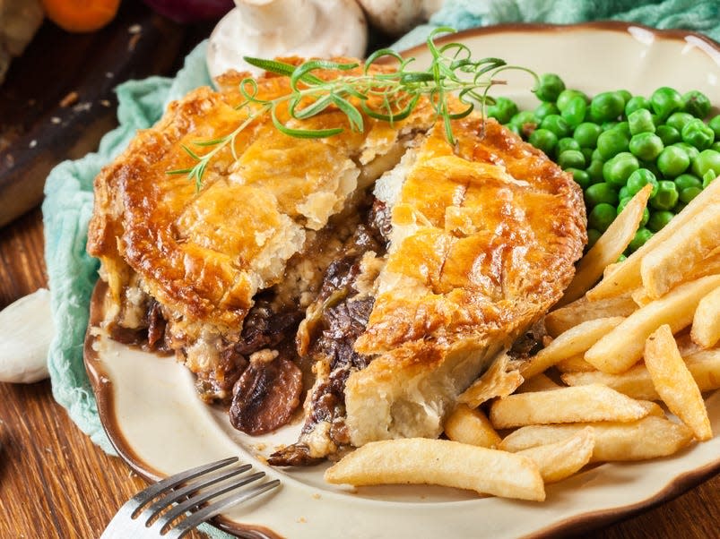 meat pie cut open with filling showing, chips, and peas