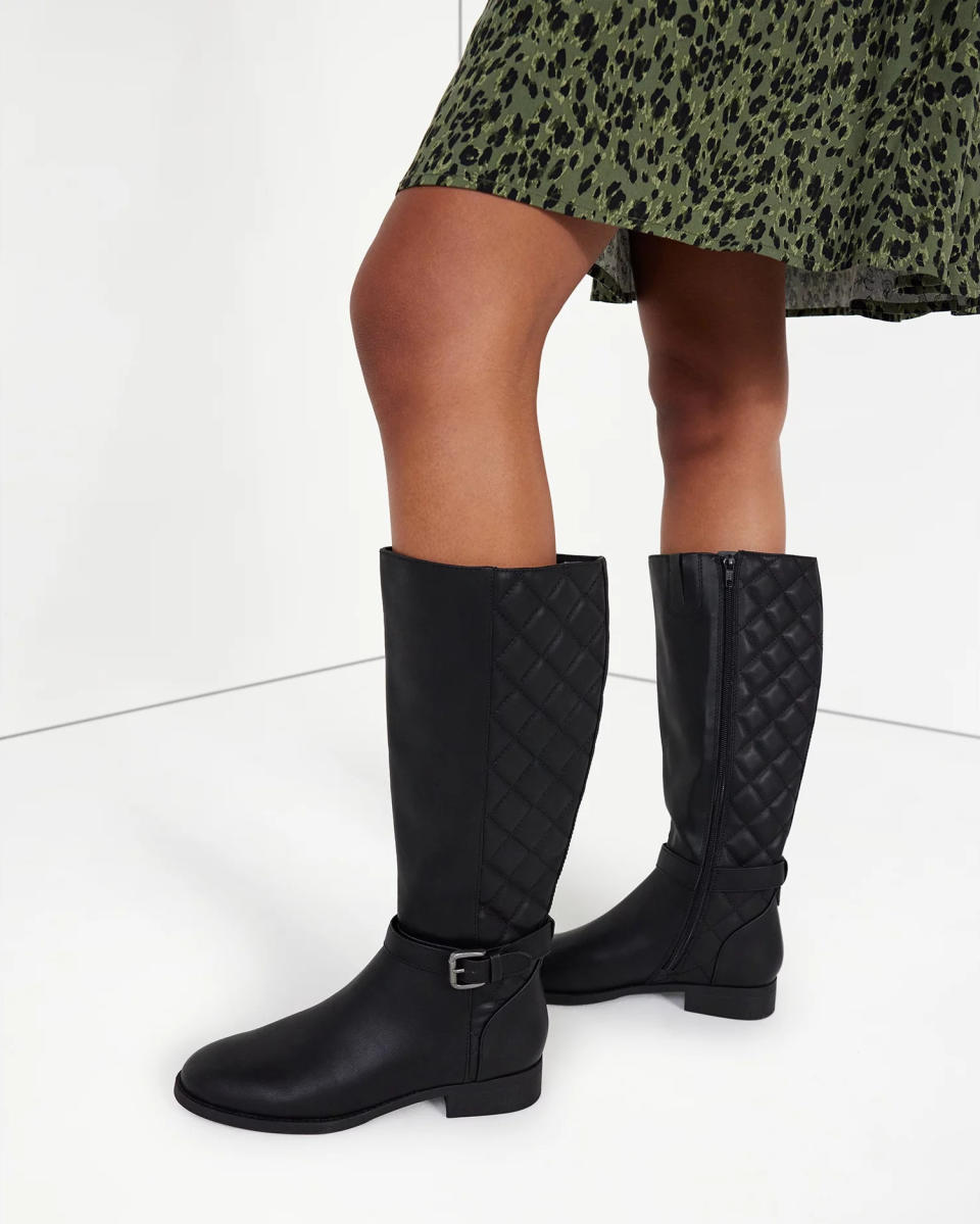 A model wearing the boots in black, which buckle detail around the ankle