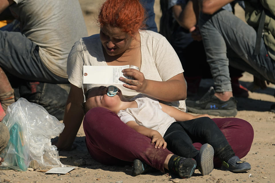 woman shields her child from the sun as she and other migrants wait to be processed by the U.S. Customs and Border Patrol after they crossed the Rio Grande and entered the U.S. from Mexico, Thursday, Oct. 19, 2023, in Eagle Pass, Texas. Starting in March, Texas will give police even broader power to arrest migrants while also allowing local judges to order them out of the U.S. under a new law signed by Republican Gov. Greg Abbott. (AP Photo/Eric Gay)