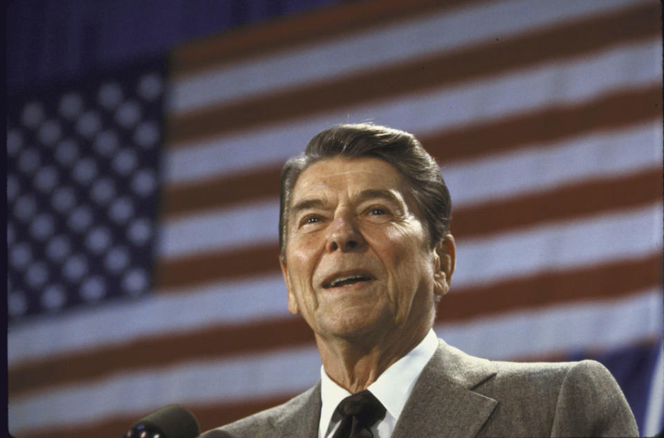 Ronald Reagan speaking at a podium with the United States flag in the background