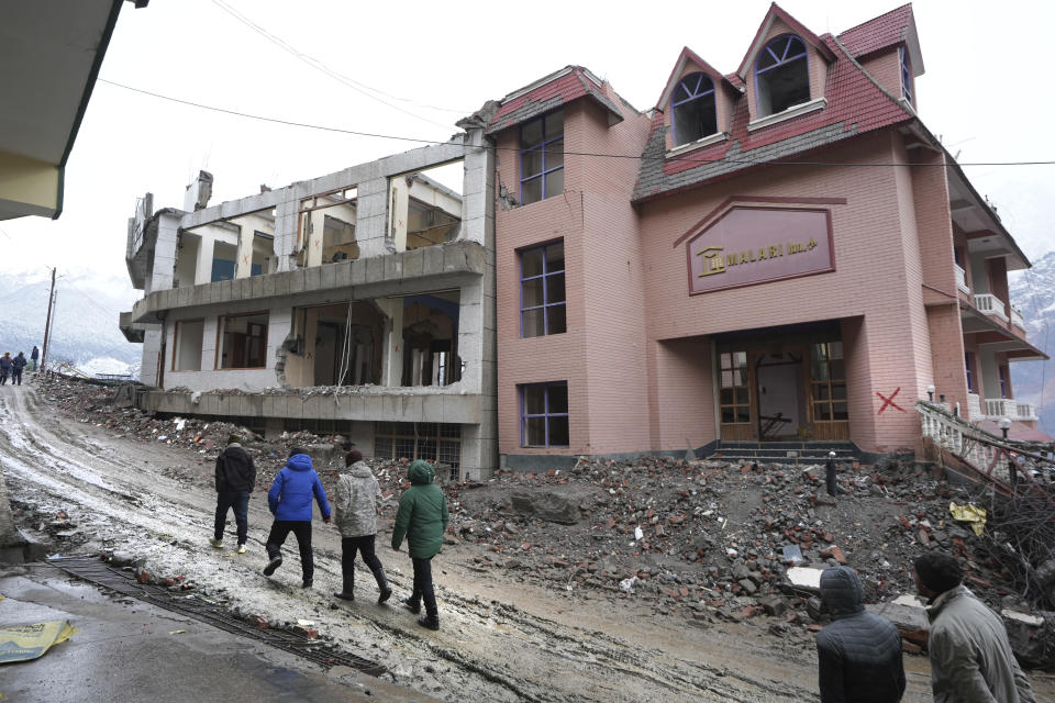 Residents walk past a demolished hotel, in Joshimath, India's Himalayan mountain state of Uttarakhand, Jan. 20, 2023. For months, residents in Joshimath, a holy town burrowed high up in India's Himalayan mountains, have seen their homes slowly sink. They pleaded for help, but it never arrived. In January however, their town made national headlines. Big, deep cracks had emerged in over 860 homes, making them unlivable. (AP Photo/Rajesh Kumar Singh)