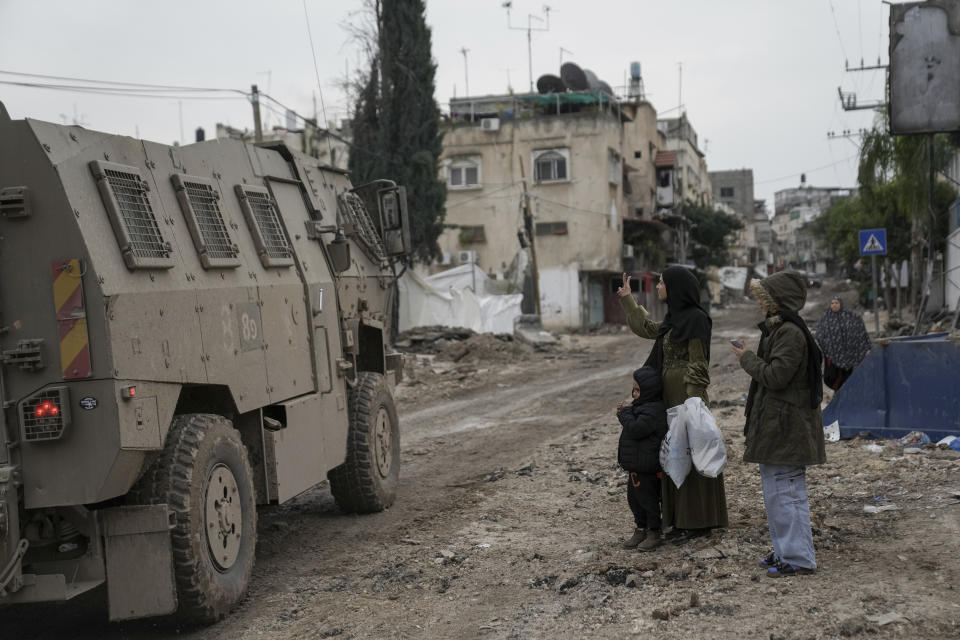 Una mujer palestina hace una "v" con sus dedos al paso de un vehículo militar israelí durante una redada en el campo de refugiados de Tulkarem, en Cisjordania, el 17 de enero de 2024. (AP Foto/Nasser Nasser)