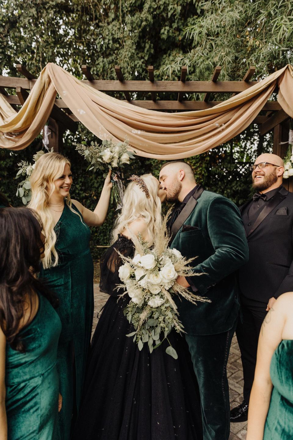 A bride and groom kiss as their bridal party celebrates around them.