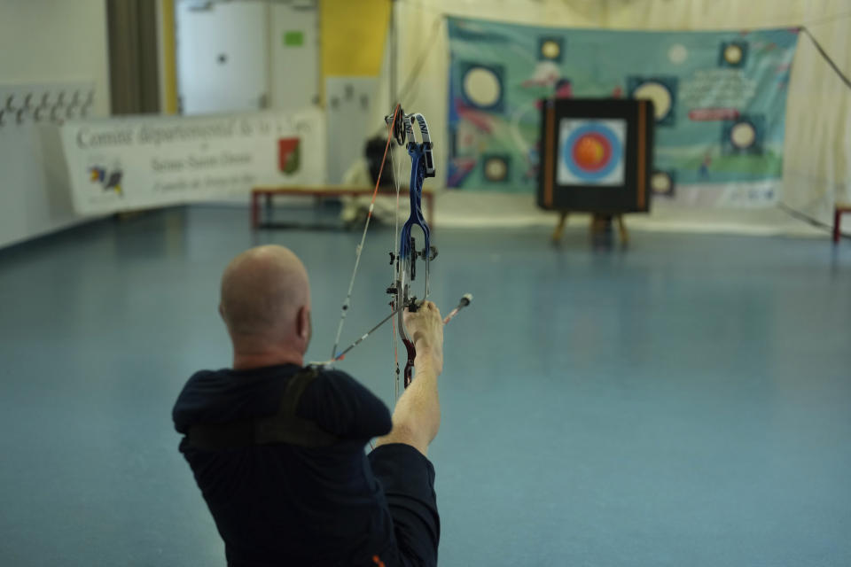 Archer Matt Stutzman of United States holds the bow with his foot during a performance in a Paris school, in Paris, Wednesday, Oct. 4, 2023. Visiting France's capital before Paralympic tickets go on sale next week, Stutzman dropped by a Paris school on Wednesday and wowed its young pupils with his shooting skills. (AP Photo/Thibault Camus)