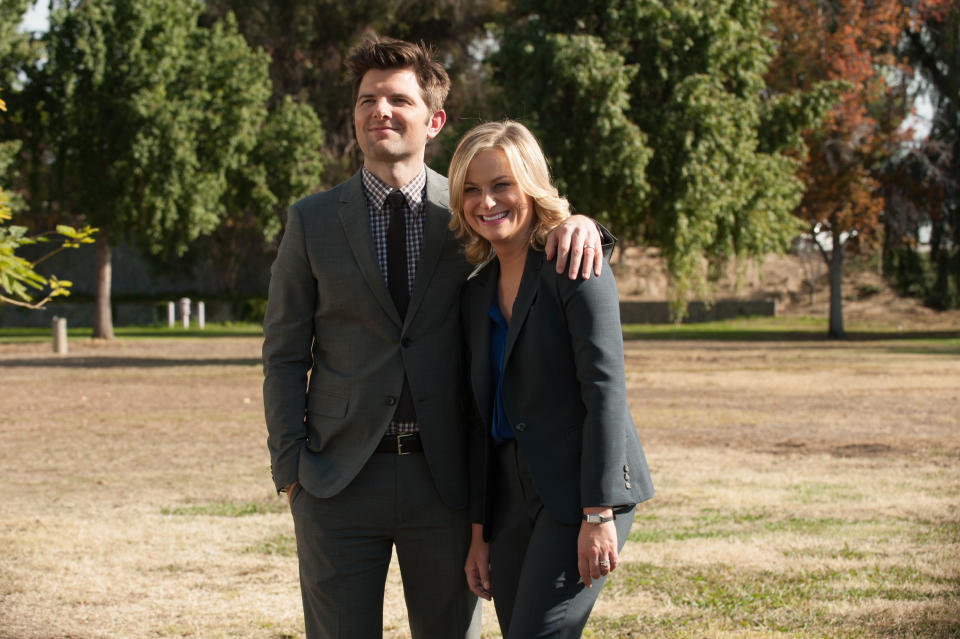 Leslie Knope and Ben Wyatt from Parks and Recreation smiling together in business attire outdoors