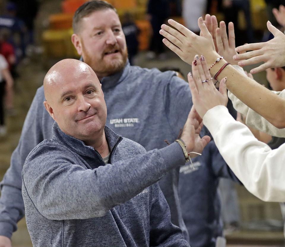 Utah State assistant coaches Andy Hill, foreground, and Chris Haslam high-five Aggie fans following the USU’s win over ETSU at the Spectrum in Logan on Dec. 22, 2023. Hill was on the University of Utah staff when Martinez was a Runnin’ Ute. | Jeff Hunter