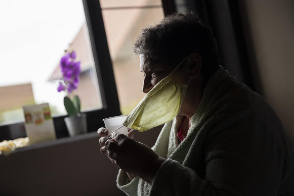 In this photo taken on Wednesday, April 29, 2020, Diane Wanten, 61, removes her mouth mask to drink water as she recuperates in quarantine at her son's house in Alken, Belgium. Wanten was recently released into home quarantine after being treated for two weeks at the Jessa Hospital ICU ward for COVID-19 coronavirus patients. (AP Photo/Francisco Seco)