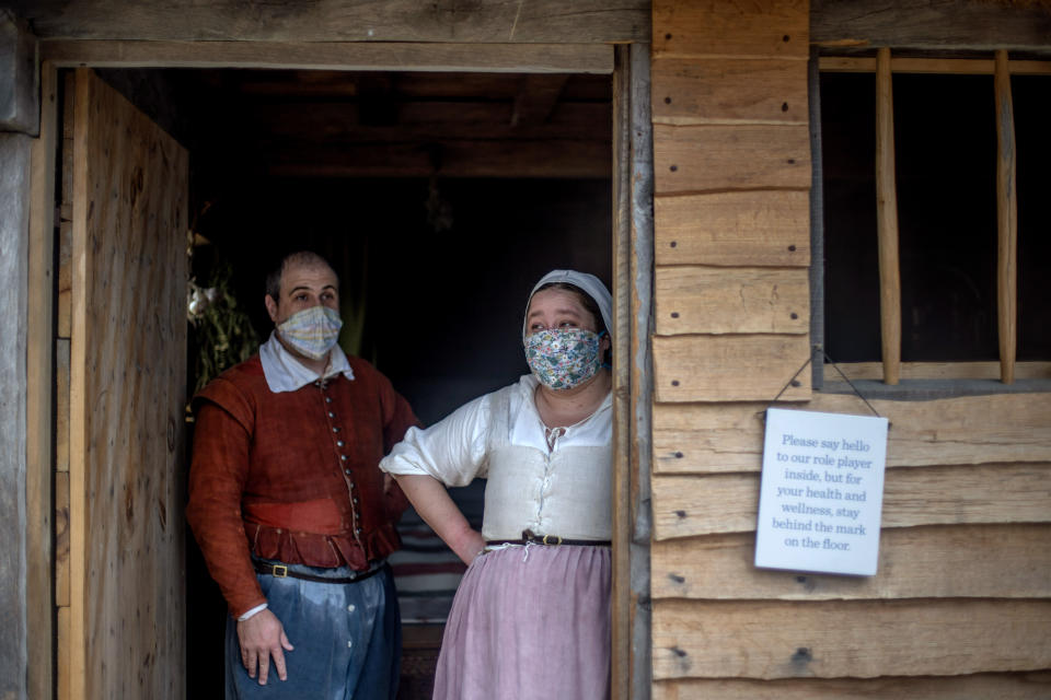 Museum educators Doug Blake, left, and Alexandra Cervenak, playing the roles of Pilgrims William and Alice Bradford, wait for visitors at Plimoth Plantation, a reconstructed Pilgrim settlement and living history exhibit, Wednesday, Aug. 12, 2020, in Plymouth, Mass. After more than two months at sea, the Pilgrims landed at the place the Wampanoags called Patuxet, meaning "at the little falls." When they disembarked from the leaky, fetid carrack, they stepped foot on a land already cleared by death's scythe. (AP Photo/David Goldman)