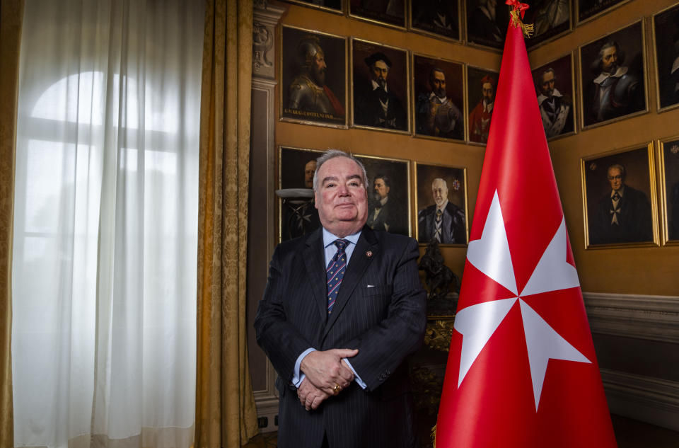 John Dunlap poses with the Sovereign Military Order of Malta's flag in the Chapter Room at their headquarters in Rome, Friday, March 31, 2023. Dunlap, a Canadian lawyer who found his vocation ministering to AIDS patients in Harlem has been elected Wednesday, May 3, 2023, the grand master of the Knights of Malta, the first non-European and first non-aristocratic head of the ancient Catholic order that provides humanitarian aid around the world. (AP Photo/Domenico Stinellis)