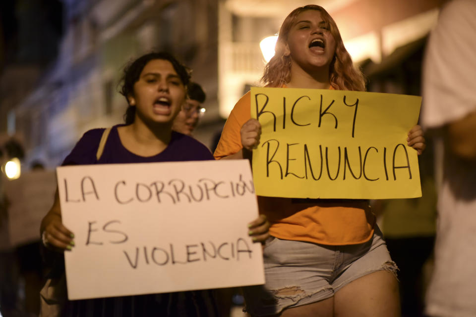 Demonstrators holding signs that read in Spanish "Corruption is violence" and "Ricky renounce", protest near the executive mansion denouncing a wave of arrests for corruption that has shaken the country and demanding the resignation of Gov. Ricardo Rosello, in San Juan, Puerto Rico, Thursday, July 11, 2019. Puerto Rico's former secretary of education and 5 other people have been arrested on charges of steering federal money to unqualified, politically connected contractors. U.S. Attorney for Puerto Rico Rosa Emilia Rodríguez said Gov. Rossello was not involved in the investigation. (AP Photo/Carlos Giusti)
