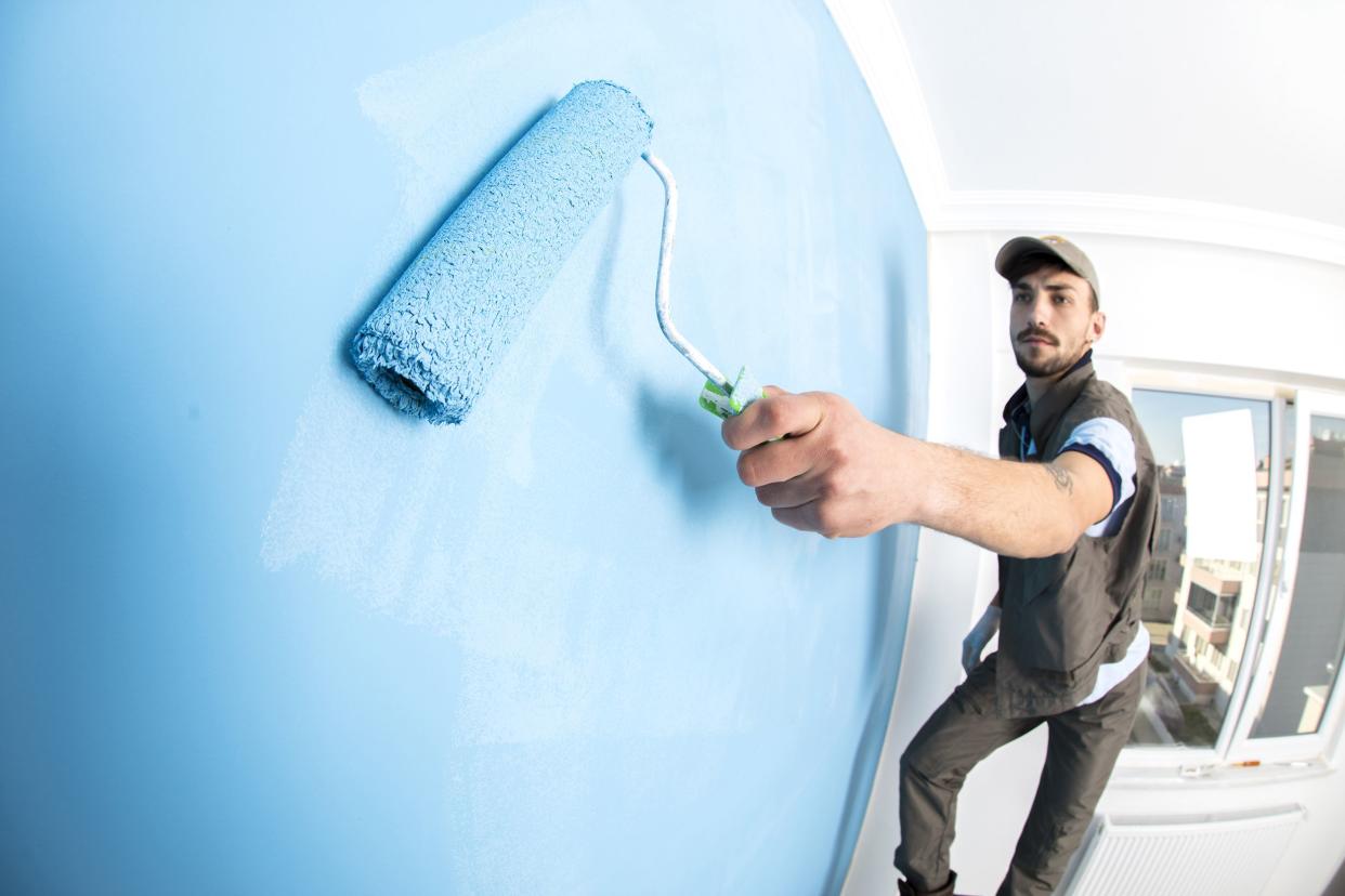 young man painting a wall blue with a roller