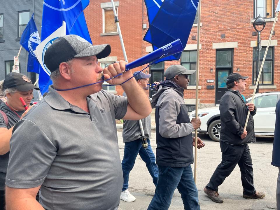 Mark Langlois, a defect specialist at the Owens Illinois plant in Montreal, said his colleagues call him 'red-lobster face' because of the colour his skin turns when he has been working near the blistering hot machinery on the factory floor. Here, he blows a horn during a solidarity march to support the workers' strike on Friday, June 12. 2023. 