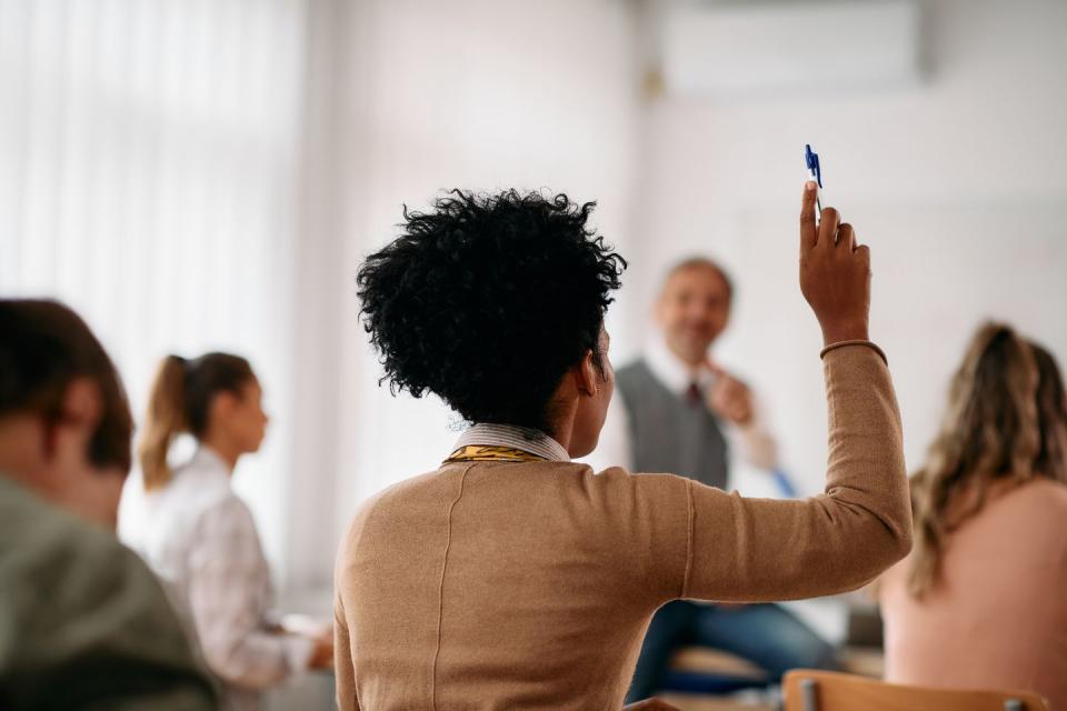 back view of african american student raising her arm to answer a question during lecture in the classroom