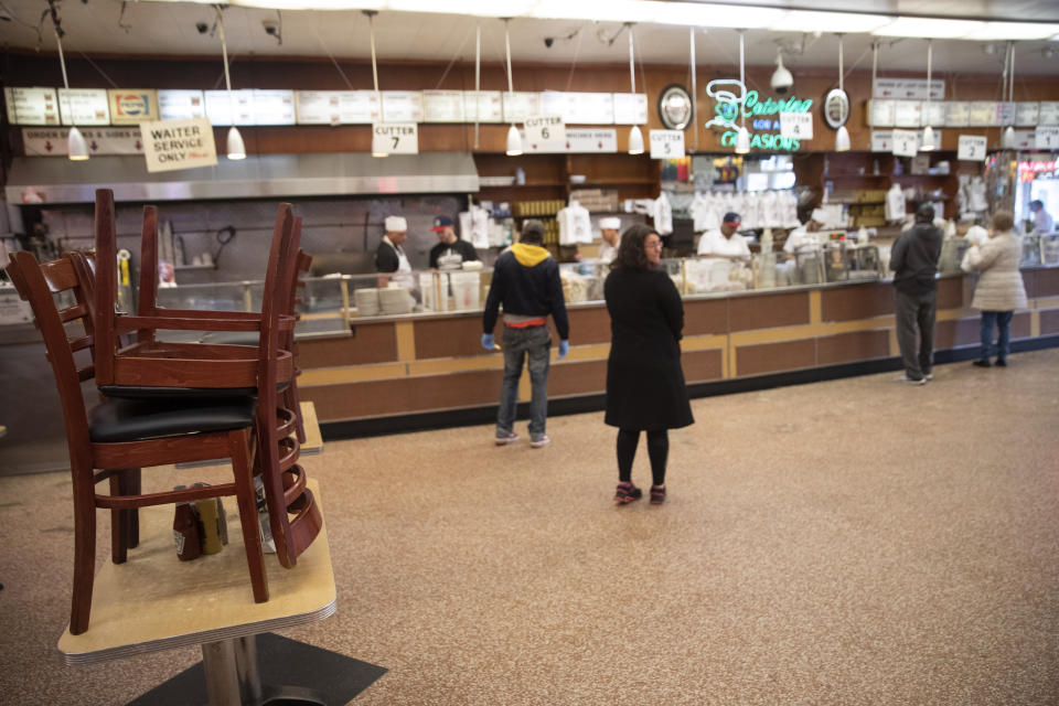 I this March 19, 2020 photo, chairs are stacked on the table where the Meg Ryan and Billy Crystal filmed the famous scene from the movie "When Harry Met Sally," as customers wait for take out orders at Katz's Delicatessen on the Lower East Side of New York. The iconic eatery is only open for take out and delivery orders due to the coronavirus outbreak. (AP Photo/Mary Altaffer)