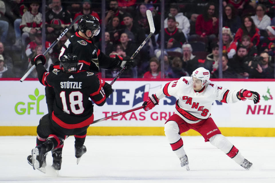 Ottawa Senators center Tim Stutzle (18) and Ottawa Senators left wing Brady Tkachuk (7) collide as Carolina Hurricanes center Sebastian Aho (20) looks towards the puck during the first period of an NHL hockey match in Ottawa, Ontario, on Tuesday, Dec. 12, 2023. (Sean Kilpatrick/The Canadian Press via AP)