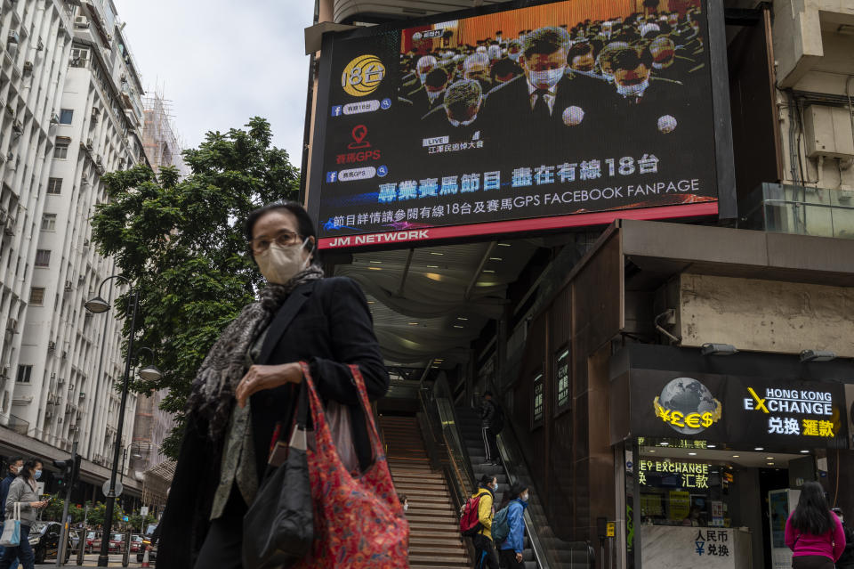 A woman wearing mask walks past an outdoor screen displaying a live broadcast of the memorial service for late former Chinese President Jiang Zemin in Hong Kong, Tuesday, Dec. 6, 2022. A formal memorial service was held Tuesday at the Great Hall of the People, the seat of the ceremonial legislature in the center of Beijing. (AP Photo/Vernon Yuen)