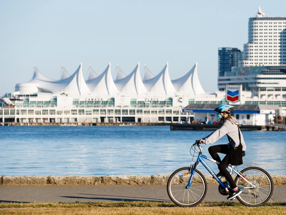 A woman wearing a protective mask rides a bicycle along the seawall at Stanley Park on August 04, 2020 in Vancouver, Canada.