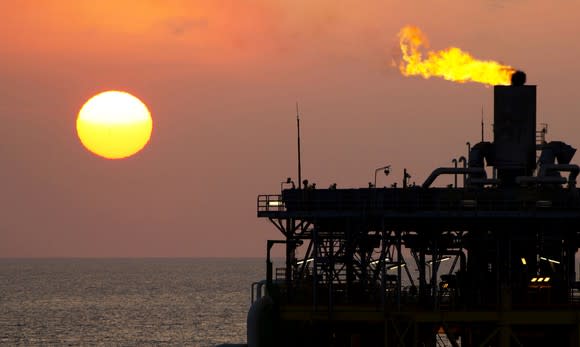 Gas flaring off an offshore oil platform with the sun in the background.