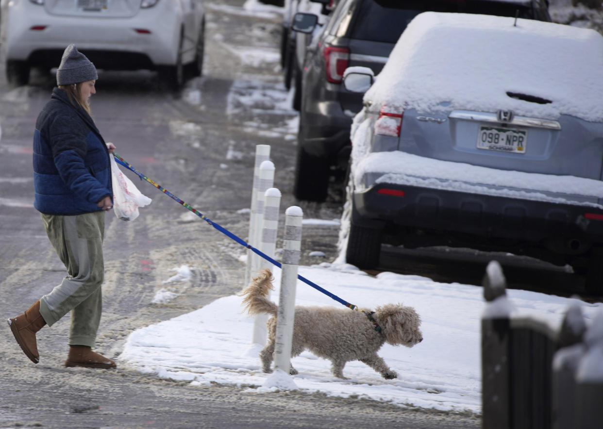 A woman walks a dog after a storm swept over the region and deposited the first snow of the season Friday, Dec. 10, 2021, in Denver. (AP Photo/David Zalubowski)