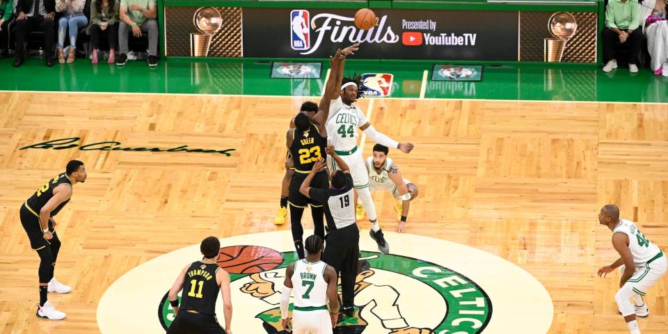 The Warriors and Celtics jump for the ball at the center of the court at the beginning of an NBA Finals game.